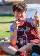 Rio Rancho junior rugby player seated on the grass giving a thumbs up